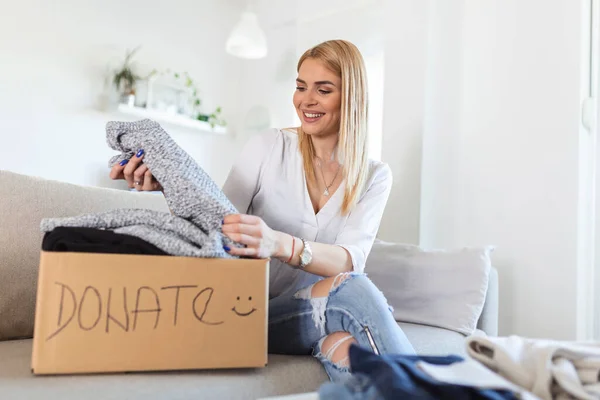 Happy Blond Young Woman Sit Couch Stuck Clothes Donation Box — ストック写真