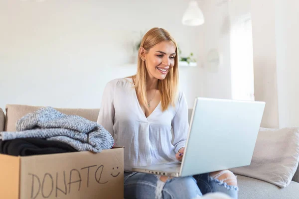 Happy Young Woman Sit Couch Stuck Clothes Donation Box Home — стоковое фото