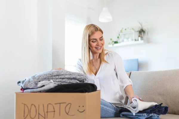 Happy Young Woman Sit Couch Stuck Clothes Donation Box Home — ストック写真