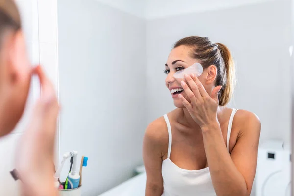 幸せな若い女性浴室と笑顔で顔マスクを適用します 美容治療を行う鏡の前で美しい女性 — ストック写真