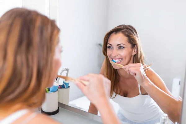 Portrait of attractive woman brushing teeth in bathroom and looking in the mirror at reflection. healthy teeth. Happy lovely young woman looking at the mirror and brushing teeth in bathroom
