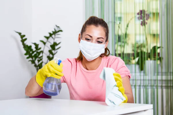 Woman with protective glove and facial mask.Health protection. Hands with yellow gloves.She sprinkling disinfectant and cleaning the table. Stay safe.
