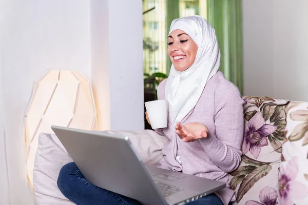 Muslim woman working with computer. Arab Young business woman sitting at her desk at home, working on a laptop computer and drinking coffee or tea. Muslim woman working at a home and using computer.