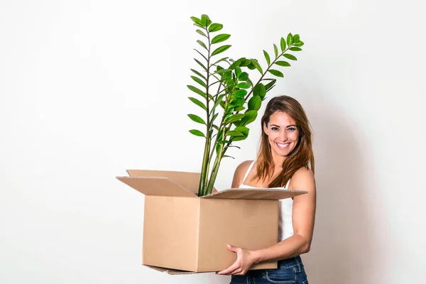 The young happy woman is moving into a new house. She brings a box with her favorite plant to her new home.