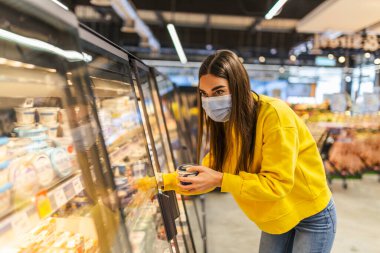 Coronavirus zatürree salgını sırasında tek kullanımlık tıbbi maske takan genç bir kadın süpermarkette alışveriş yapıyor. Salgın sırasında tedbirlerin korunması ve önlenmesi.