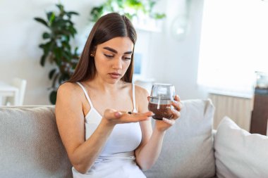 Korkunç acıdan acı çekme kavramı. Güzel, üzgün, üzgün, mutsuz, sorunlu, siyah saçlı, sıradan kıyafetler giyen zayıf kadın bir kanepede oturup hap alıyor.