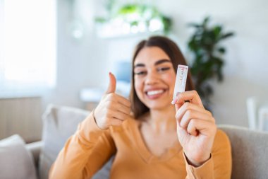 Negatif bir test cihazını tutan kadının yakın plan fotoğrafı. Negatif Coronavirus 'unu gösteren mutlu genç kadın - Covid-19 hızlı testi. Teste odaklan. Coronavirüs.