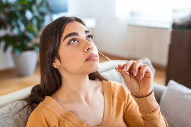 Kadın evde koronavirüs PCR testi yaparken pamuk çubuğu kullanıyor. Coronavirus hızlı tanı testi uygulayan bir kadın. Evde genç bir kadın COVID-19 için burun çubuğu kullanıyor..