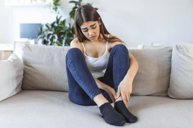 Gün boyunca kanepede otururken ellerin şişmiş ayaklara masaj yapıyor. Bacağındaki ağrıdan muzdarip beyaz bir kadının fotoğrafı. Ofiste bütün gün çalıştıktan sonra bacaklarına masaj yapan bir kadın.