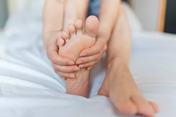 Foot Pain woman sitting on the bed holding her feet at home having painful feet and stretching muscles fatigue To relieve pain. Health concept.