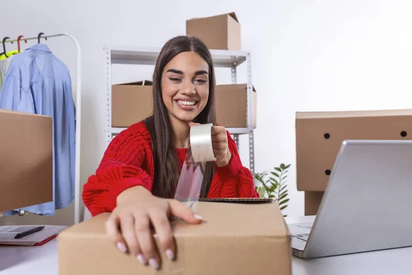 Young woman, owener of small business packing product in boxes, preparing it for delivery. Women packing package with her products that she selling online