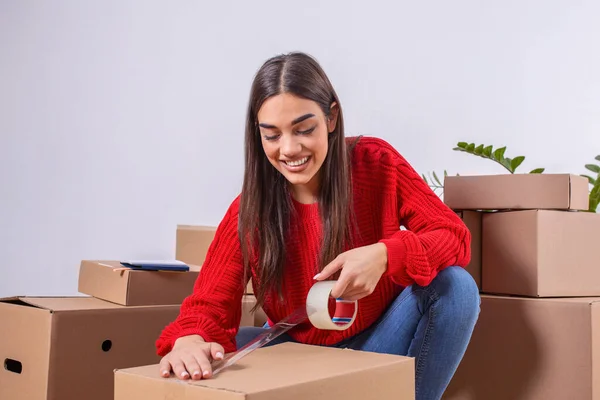 Close up of Young woman packing cardboard box. Moving house concept. Beautiful girl taping up a cardboard box with adhesive tape.