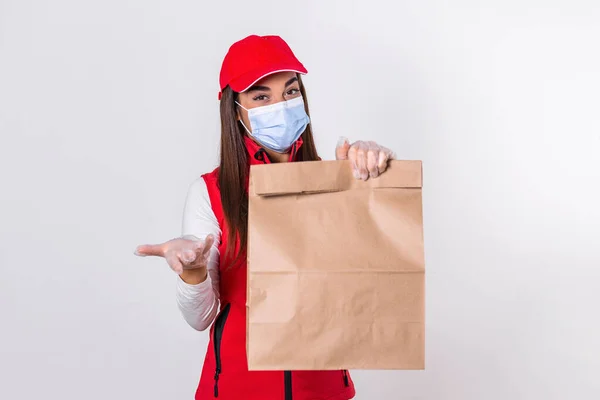 Delivery woman employee in red cap t-shirt uniform mask glove hold craft paper packet with food isolated on white background studio Service quarantine pandemic coronavirus virus 2019-ncov concept