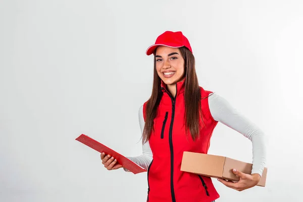 Delivery person delivering packages holding clipboard and package smiling happy in red uniform. Beautiful young woman professional courier isolated on white background