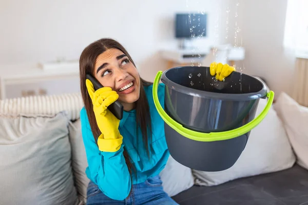 Shocked Woman Calling Plumber While Collecting Water Leaking From Ceiling Using Utensil