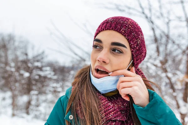 Don\'t touch your face, stop spreading Coronavirus. Young woman touching her mouth with dirty hand. Avoid touching your face. Woman putting down face mask rubbing her lip outdoor.