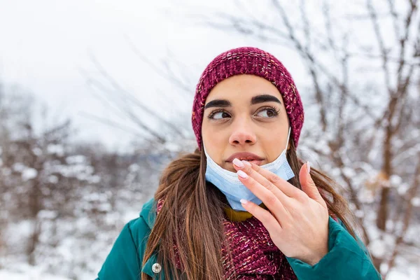 Don\'t touch your face, stop spreading Coronavirus. Young woman touching her mouth with dirty hand. Avoid touching your face. Woman putting down face mask rubbing her lip outdoor.