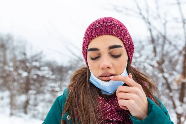 Don't touch your face, stop spreading Coronavirus. Young woman touching her mouth with dirty hand. Avoid touching your face. Woman putting down face mask rubbing her lip outdoor.