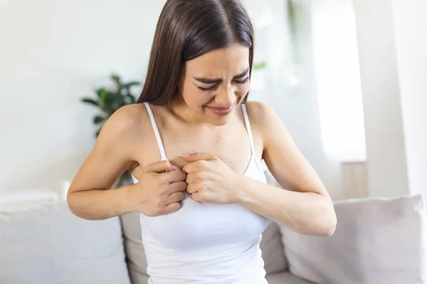 Woman sitting with strong chest pain and hands touching her chest while having trouble at home, Heart attack or heart failure symptom