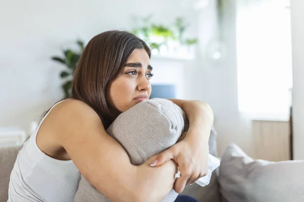 Young woman hugging pillow with depression and crying on sofa at home. Lonely millennial lady feeling stressed and hopeless, suffering from mood disorder or having psychological problem