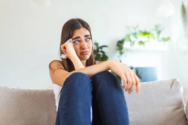 Unhappy young woman covering face with hands, crying alone close up, depressed girl sitting on couch at home, health problem or thinking about bad relationships, break up with boyfriend, divorce