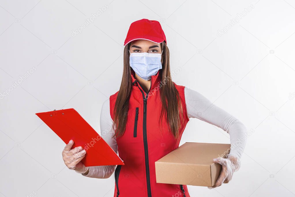 Delivery person delivering packages holding clipboard and package smiling happy in red uniform. Beautiful young woman wearing medical mask and gloves professional courier isolated on white background