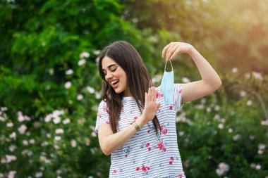 Woman saying stop to her mask. young happy girl looking at protective medical mask, take off remove mask from her face. End of pandemic coronavirus concept. NCoV, Covid 19. Pollen allergy at spring