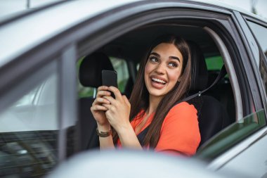 Nice beautiful young woman smile and use mobile phone touching the screen inside the car while travel. modern concept of search hings and contact friends when you are away. daily use of smartphone