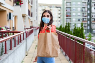 Young woman volunteer with a medical mask is holding a paper bag with food and vegetables. Donation, helping people in quarantine, coronavirus. Delivery shopping during Covid 19 outbreak.