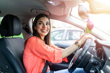 Cute young lady happy driving car. Image of beautiful young woman driving a car and smiling. Portrait of happy female driver steering car with safety belt on