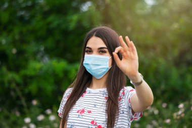 Young woman wearing medical face mask outdoors. Woman Wearing Protective Mask and Showing OK sign. Woman wearing surgical mask for corona virus