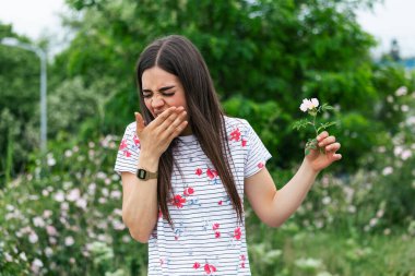 Young woman with Pollen allergy holding a flower and saying no.. Young woman with pollen and grass allergies. Flowering trees in background. Spring Seasonal allergies and health problems.