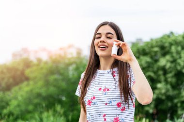 Woman applies nasal spray. Young woman using nose spray for her pollen and grass allergies (Allergy relief) Flowering trees in background. Spring Seasonal allergies and health problems.