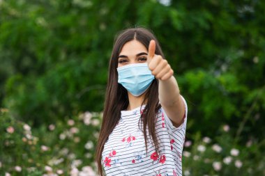 Coronavirus ve anti-smog 'u önlemek için yüz koruyucu maske takan genç kadın portresi. Yüz maskesi takan genç bir kadının portresi. Başparmak yukarı.