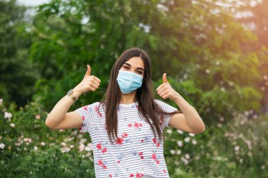 Woman suffer from sick and wearing face mask. Girl, young woman in protective sterile medical mask on her face looking at camera an showing thumb up sign.