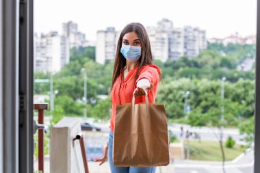 Contactless delivery of goods during Covid 19, coronavirus pandemic. The food delivery courier is holding a large paper bag in her hands. Woman with medical mask delivering food.