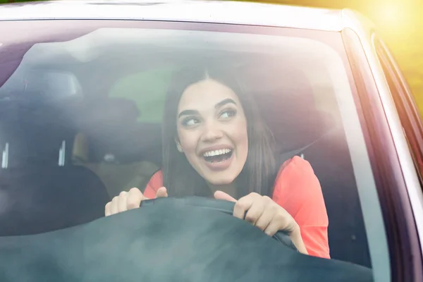 Happy brunette woman driving a car. Portrait of beautiful caucasian woman with toothy smile and brown hair driving car. Hand on steering wheel. Young woman driving a car in the city