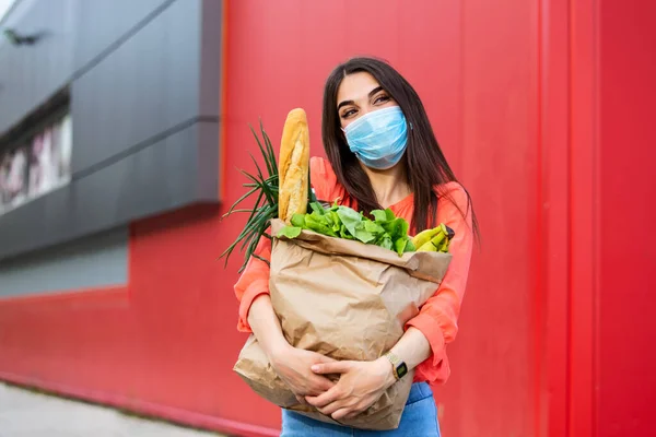 Buyer wearing a protective mask.Shopping during the Covid 19, Coronavirus pandemic quarantine. Woman in medical mask holds a paper bag with food, fruits and vegetables