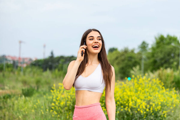 Portrait of a young woman in sportswear talking on phone outdoors while taking break between training,