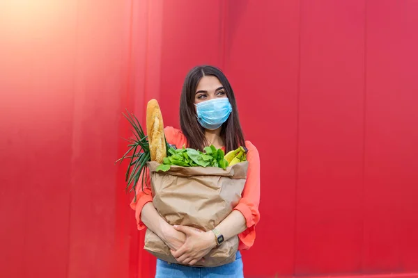 Buyer wearing a protective mask.Shopping during the Covid 19, Coronavirus pandemic quarantine. Woman in medical mask holds a paper bag with food, fruits and vegetables