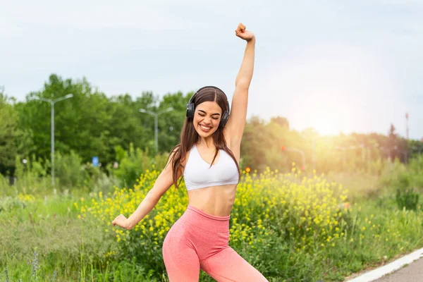 Beautiful sporty woman excited after she completed her exercise. Beautiful female runner standing outdoors with her hands in the air excited