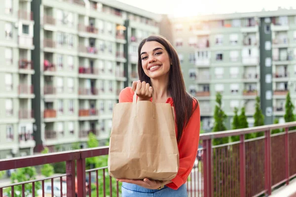 Woman delivering food in paper bag.Female volunteer holding groceries in the house porch. Delivery food service at home. Courier delivered the order no name bag with food.