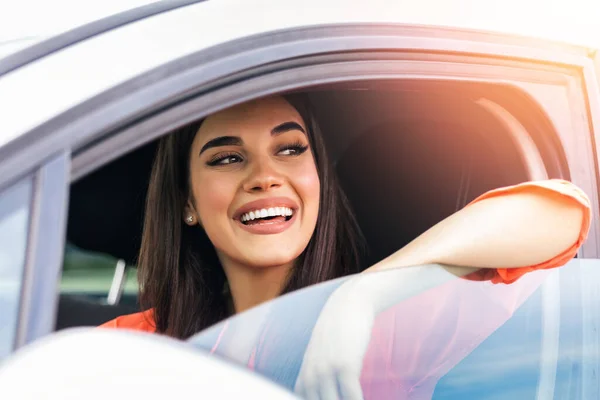 Young woman sitting in a car. Happy woman driving a car and smiling. Portrait of happy female driver steering car with safety belt. Cute young lady happy driving car.