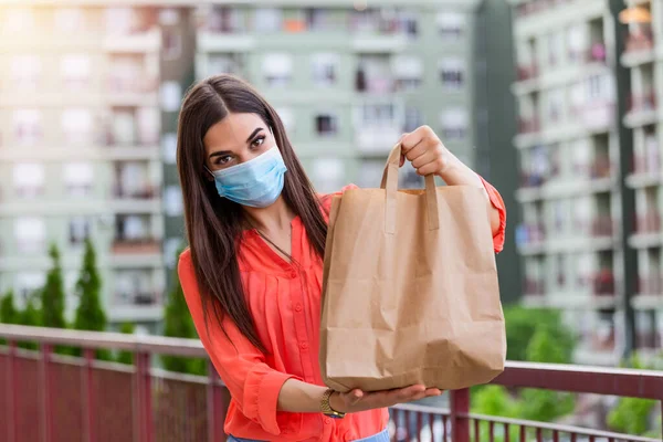 Young woman volunteer with a medical mask is holding a paper bag with food and vegetables. Donation, helping people in quarantine, coronavirus. Delivery shopping during Covid 19 outbreak.