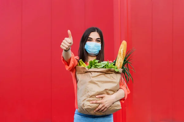 Buyer wearing a protective mask.Shopping during the Covid 19, Coronavirus pandemic quarantine. Woman in medical mask holds a paper bag with food, fruits and vegetables