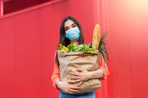 Buyer wearing a protective mask.Shopping during the Covid 19, Coronavirus pandemic quarantine. Woman in medical mask holds a paper bag with food, fruits and vegetables