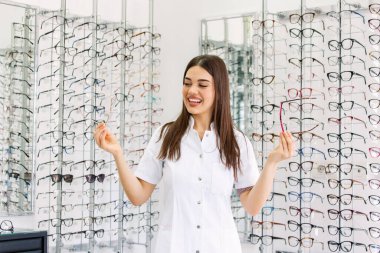 Göz hastalıkları Kliniği çekici genç kadın doktor. Doktor göz doktoruna raflar farklı gözlük ile yakın duruyor.