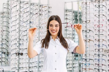 Göz hastalıkları Kliniği çekici genç kadın doktor. Doktor göz doktoruna raflar farklı gözlük ile yakın duruyor.