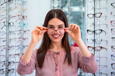 Health care, eyesight and vision concept - happy woman choosing glasses at optics store. clipart