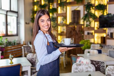 Happy waitress holding tray with cup of coffee, working in cafeteria and serves the table